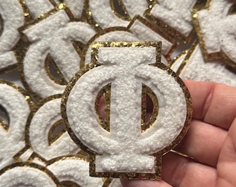 May include: A white felt Greek letter Phi with a gold glitter outline. The letter is surrounded by other Greek letters.