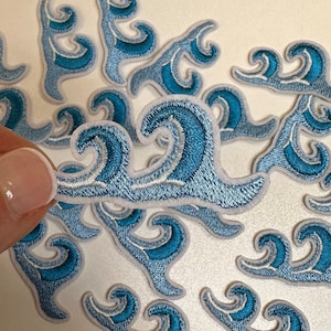 May include: A collection of blue and white wave-shaped iron-on patches. The patches are arranged in a random pattern on a white surface.