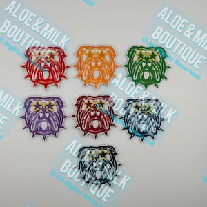 May include: A collection of colorful bulldog patches. Each patch features a bulldog head with star accents and a spiked collar. The patches are in various colors, including red, orange, green, purple, maroon, blue, and black.