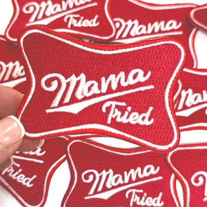 May include: A close-up of several red embroidered patches with white stitching. The patches are shaped like a beer bottle and say "Mama Fried" in a retro font.