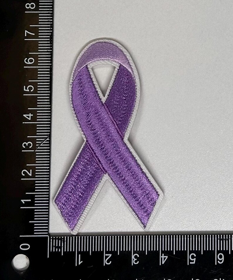May include: Purple ribbon embroidered patch with white outline. The ribbon is tied in a knot and is approximately 2 inches in length.