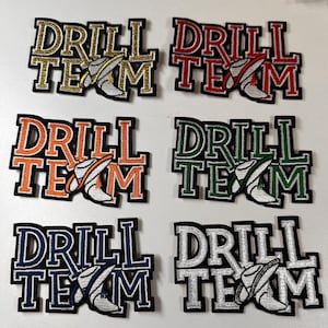 May include: Six embroidered patches with the text "DRILL TEAM" in different colors. The patches feature a white boot with a gold trim and a gold star on the side.