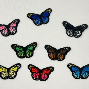 May include: A collection of embroidered butterfly patches in various colors, including pink, blue, green, brown, yellow, and red. Each patch features a black outline and detailed wing patterns, suitable for fabric embellishment or crafting projects.