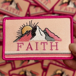 May include: Pink and white embroidered patch with a mountain range and a sun rising over the mountains. The word "FAITH" is embroidered in pink below the mountains.