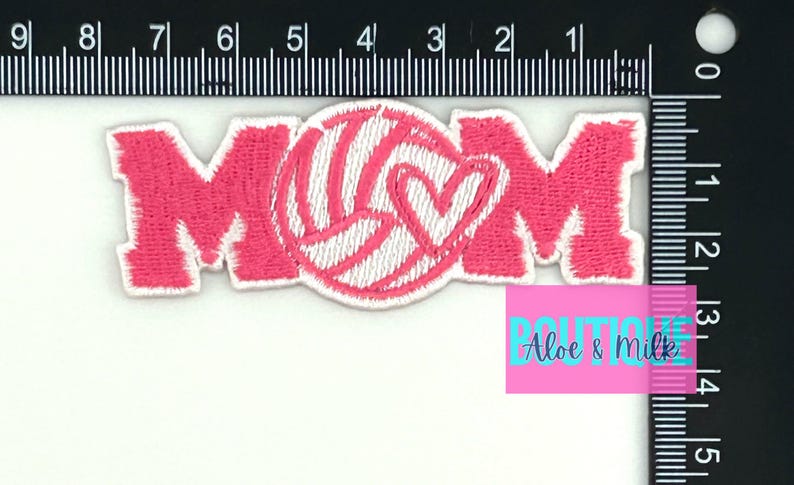 Pu&ograve; includere: Toppa da stiro ricamata rosa con la parola "MOM" e una pallavolo bianca con un cuore all'interno.