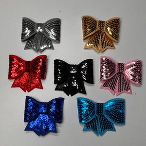 May include: Assortment of seven sequined bow patches in various colors, including red, black, gold, pink, blue, silver, and teal.