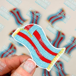 May include: A blue and red striped towel with yellow fringe. The towel is embroidered with a wavy pattern.