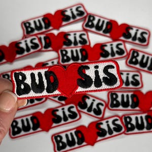 May include: A set of 12 iron-on patches with a red heart and the text "BUD SIS" in black and white lettering.