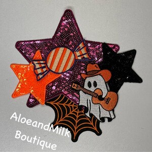 May include: A set of five Halloween-themed iron-on patches. The patches include a pink sequined star, an orange sequined star, a black sequined star, a candy cane, and a ghost playing a guitar. The patches are perfect for adding a spooky touch to clothing, bags, or other accessories.