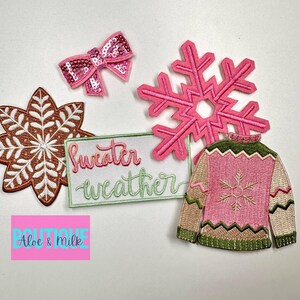 May include: Five embroidered iron-on patches with a winter theme. The patches include a pink snowflake, a brown snowflake, a pink bow, a pink sweater with a green collar and a green and brown snowflake, and a white patch with the text "sweater weather" in pink and green.