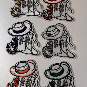 May include: Six embroidered patches featuring a white cowboy hat and boots with a pom-pom. The hats are trimmed with different colors: gold, red, blue, gray, orange, and green.