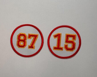 May include: Two white, round, embroidered patches with red borders. The patches feature the numbers "87" and "15" in yellow thread.