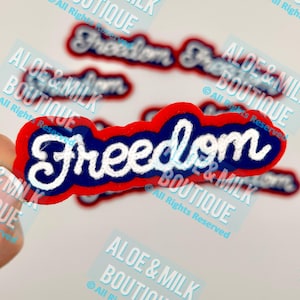 May include: Red, white, and blue embroidered patch with the word "Freedom" in a white cursive font. The patch is surrounded by a red border and a blue inner border.
