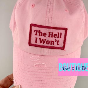 May include: Pink baseball cap with a distressed look and a red patch that says "The Hell I Won't".