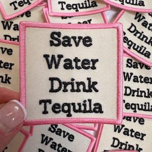 May include: A close-up of several white fabric patches with pink borders. The patches have the text "Save Water Drink Tequila" embroidered in black.
