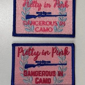 May include: Two pink and blue embroidered patches with the text "Pretty in Pink Dangerous in Camo" and a rifle with a scope.