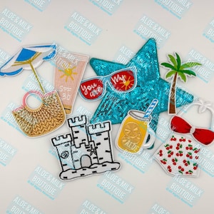 May include: A set of nine embroidered iron-on patches featuring summer vacation themes. The patches include a beach bag, a sandcastle, a palm tree, a mason jar with lemonade, a pair of sunglasses, a bottle of sunscreen, a beach umbrella, a swimsuit, and a turquoise star.