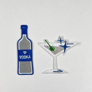 May include: Two embroidered iron-on patches, one of a bottle of vodka and the other of a martini glass with a green olive. Both patches have a white background with blue and silver accents.