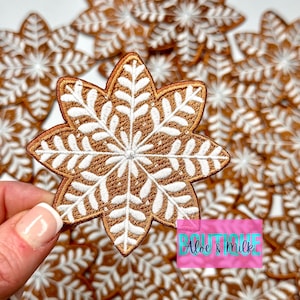May include: A close-up of a pile of brown and white snowflake-shaped iron-on patches. The patches are embroidered with a white snowflake design on a brown background. The text "Aloe & Milk" is visible in the lower right corner of the image.