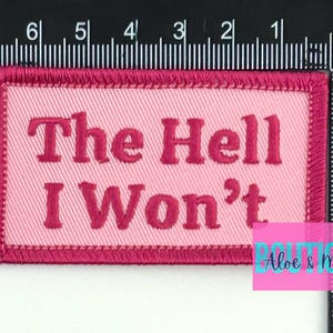 May include: Pink and red embroidered patch with the text "The Hell I Won't".