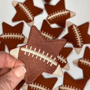May include: A set of brown star-shaped iron-on patches with a white football design. The patches are perfect for adding a sporty touch to clothing, bags, or other fabric items.