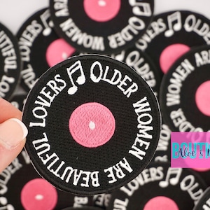 May include: A set of black and white embroidered iron-on patches with a pink record design. The patches feature the text "Older Women Are Beautiful Lovers" and a musical note.