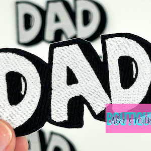 May include: White embroidered "DAD" patch with black outline. The patch is made of fabric and has a slightly puffy texture.