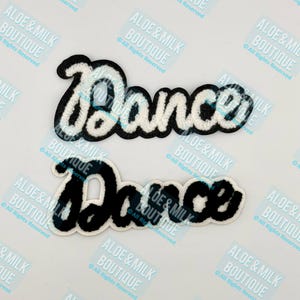 May include: Two black and white felt patches with the word "Dance" in a cursive font. The patches are on a white background.