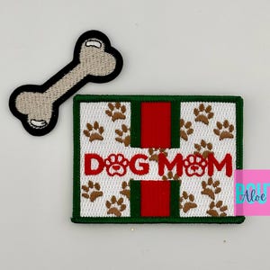 May include: Green, red, and white embroidered patch with the text "DOG MOM" and paw prints. The patch is surrounded by a green border. A white bone with a black outline is also included.