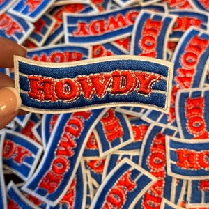 May include: A close-up of a pile of blue and white fabric patches with red embroidered lettering that says "HOWDY".