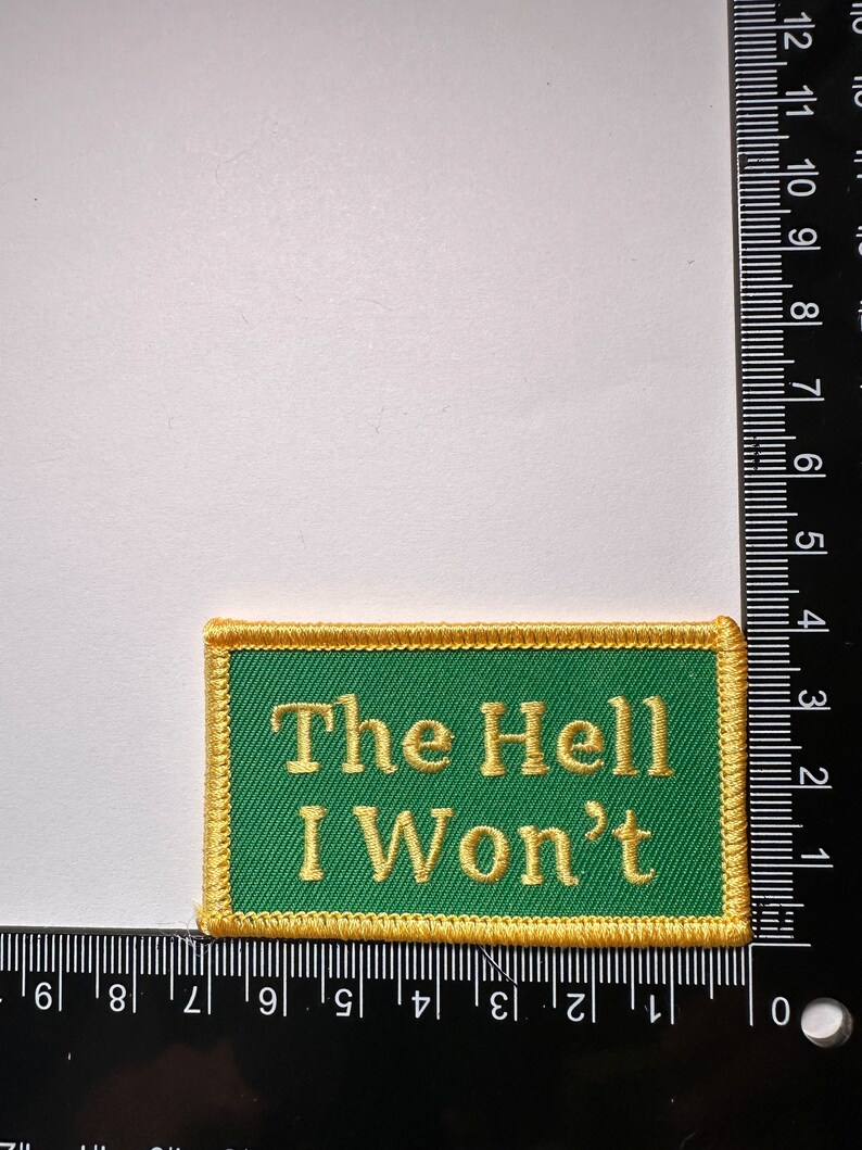 May include: A green embroidered patch with a gold border. The patch says "The Hell I Won't" in gold thread.
