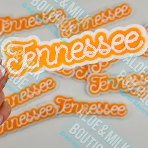 May include: Orange and white Tennessee patch with the word "Tennessee" in a cursive font. The patch has a white border and is surrounded by other similar patches.