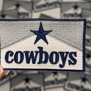 May include: A white and blue embroidered patch with a blue star and the word "cowboys" in blue lettering.