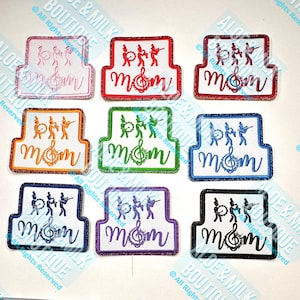 May include: Set of ten iron-on patches featuring a marching band with the word "mom" and a musical note. The patches are in various colors including pink, red, orange, green, blue, purple, and black.
