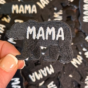 May include: A black felt iron-on patch in the shape of a bear with the word "MAMA" embroidered in white thread.