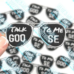 May include: A pair of black iron-on patches shaped like sunglasses. The left lens says "Talk to Me" and the right lens says "Talk Goo".