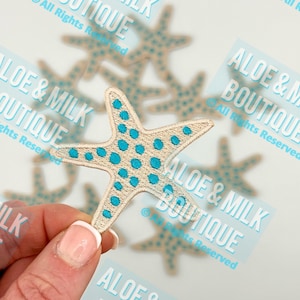 May include: A beige starfish with blue polka dots. The starfish is embroidered and has a slightly textured surface. The starfish is a popular beach-themed craft supply.