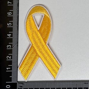 May include: A yellow ribbon embroidered patch with white stitching. The ribbon is tied in a bow shape.