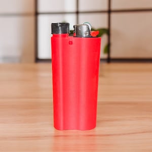 May include: A red lighter with a black top and a silver wheel. The lighter is on a wooden surface.