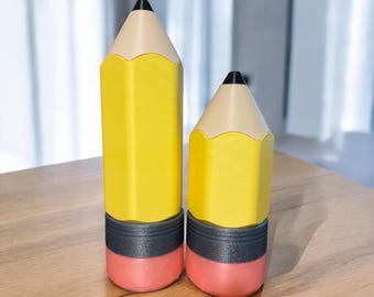 May include: Two yellow pencil-shaped containers with black and gray bands and red erasers. The containers are different sizes.