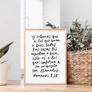 May include: A white framed print with a black handwritten quote in Spanish. The quote reads "Y sabemos que a los que aman a Dios, todas las cosas les ayudan a bien, esto es, a los que conforme a su prop&oacute;sito son llamados. Romanos 8:28"