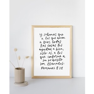 May include: A framed print with a white background and black handwritten text in Spanish. The text reads "Y sabemos que a los que aman a Dios, todas las cosas les ayudan a bien, esto es, a los que conforme a su prop&oacute;sito son llamados. Romanos 8:28"