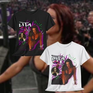 Può includere: Due t-shirt con una stampa grafica di una lottatrice. La t-shirt nera ha una stampa bianca e la t-shirt bianca ha una stampa nera. Entrambe le t-shirt mostrano il nome della lottatrice "Lita" e il logo WWF.