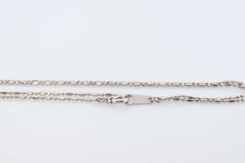May include: A silver chain necklace with a lobster clasp fastening. The chain is made of small, round beads and rectangular links.
