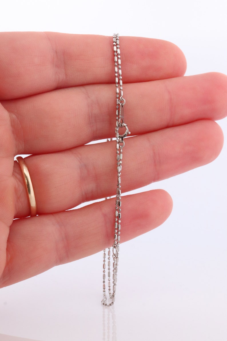 May include: A silver chain necklace with a lobster clasp fastening. The chain is made of small, round links.