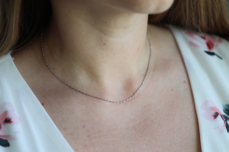 May include: A silver chain necklace worn on a person's neck. The chain is thin and delicate.