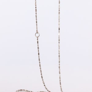 May include: A silver chain necklace with a small, round clasp. The chain is made of small, rectangular links.