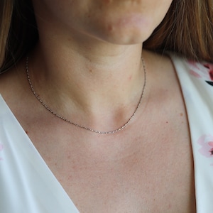 May include: A silver chain necklace worn on a person's neck. The chain is thin and delicate.