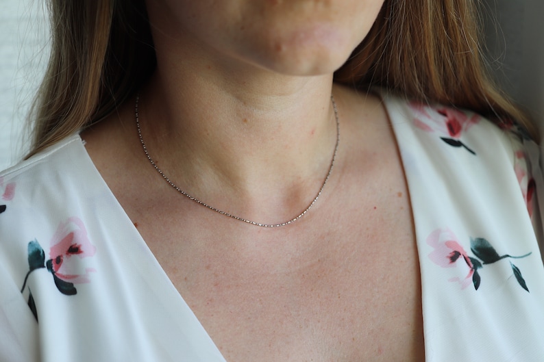 May include: A silver chain necklace worn on a person's neck. The chain is thin and delicate.