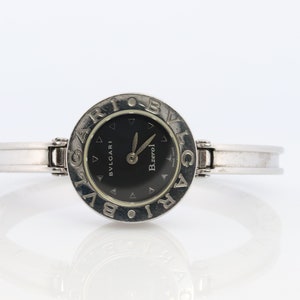 May include: A silver Bvlgari B.zero1 watch with a black face and silver hands. The watch face is surrounded by a circle of silver letters spelling out "BVLGARI".